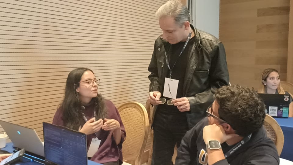 Marcos Moreira Alves standing and talking with two participants seated in front of laptops.