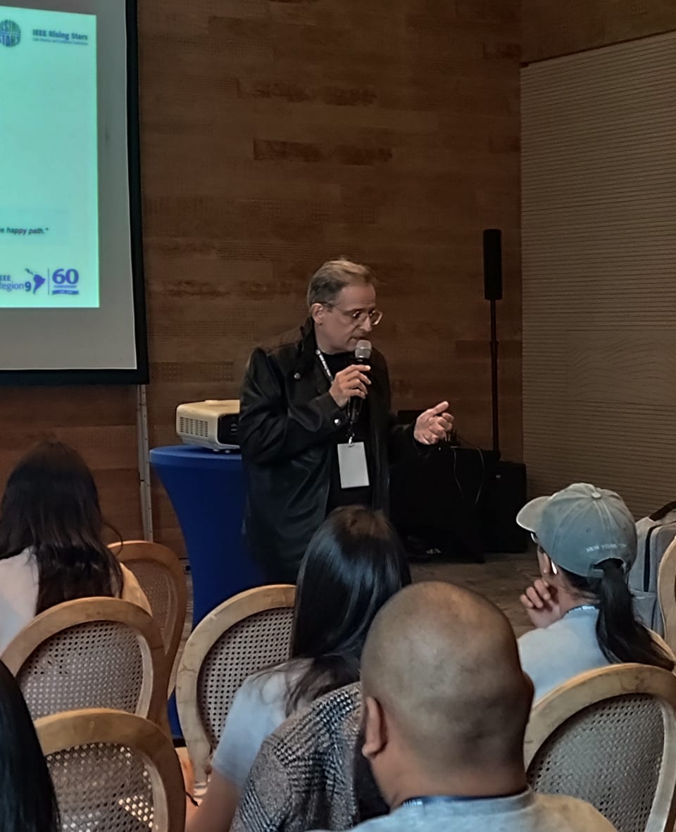 Marcos Moreira Alves at the microphone during a talk, with part of the projected slide and the audience in the background.