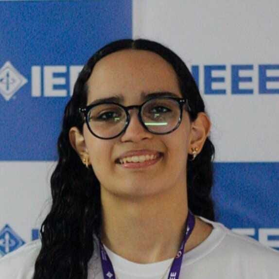 Portrait of Sophia Oliveira Alves smiling, wearing glasses, in front of an IEEE backdrop.